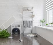 Indoor laundry room with water damage: standing water, fallen ironing board, and submerged items.