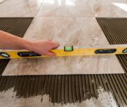 Tile installation in progress: hand using a spirit level on a beige tile.